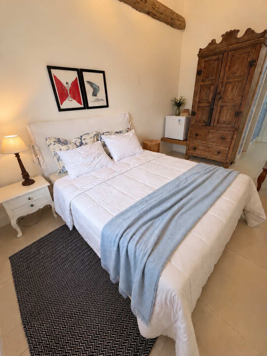Suíte 03 vista da cama: armário de madeira maciça, frigobar e quadros com um pássaro vermelho e um azul