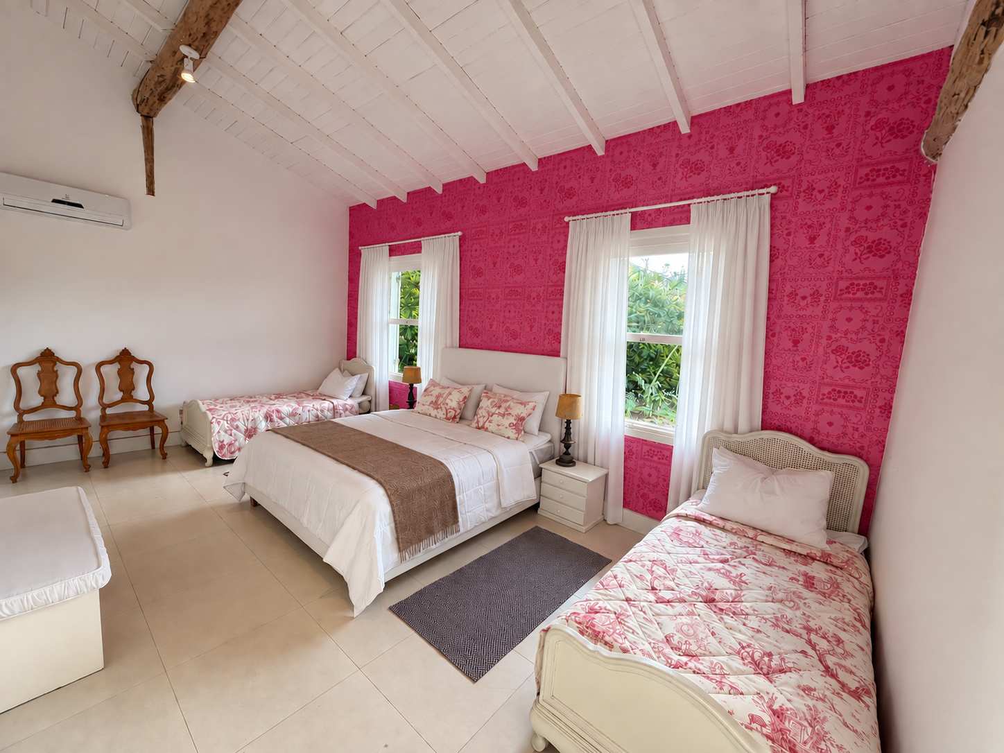 Suíte 05 em plano aberto: cama king e duas camas de solteiro no mesmo quarto, parede de papel rosa, duas janelas para o verde e teto de madeira branca com viga