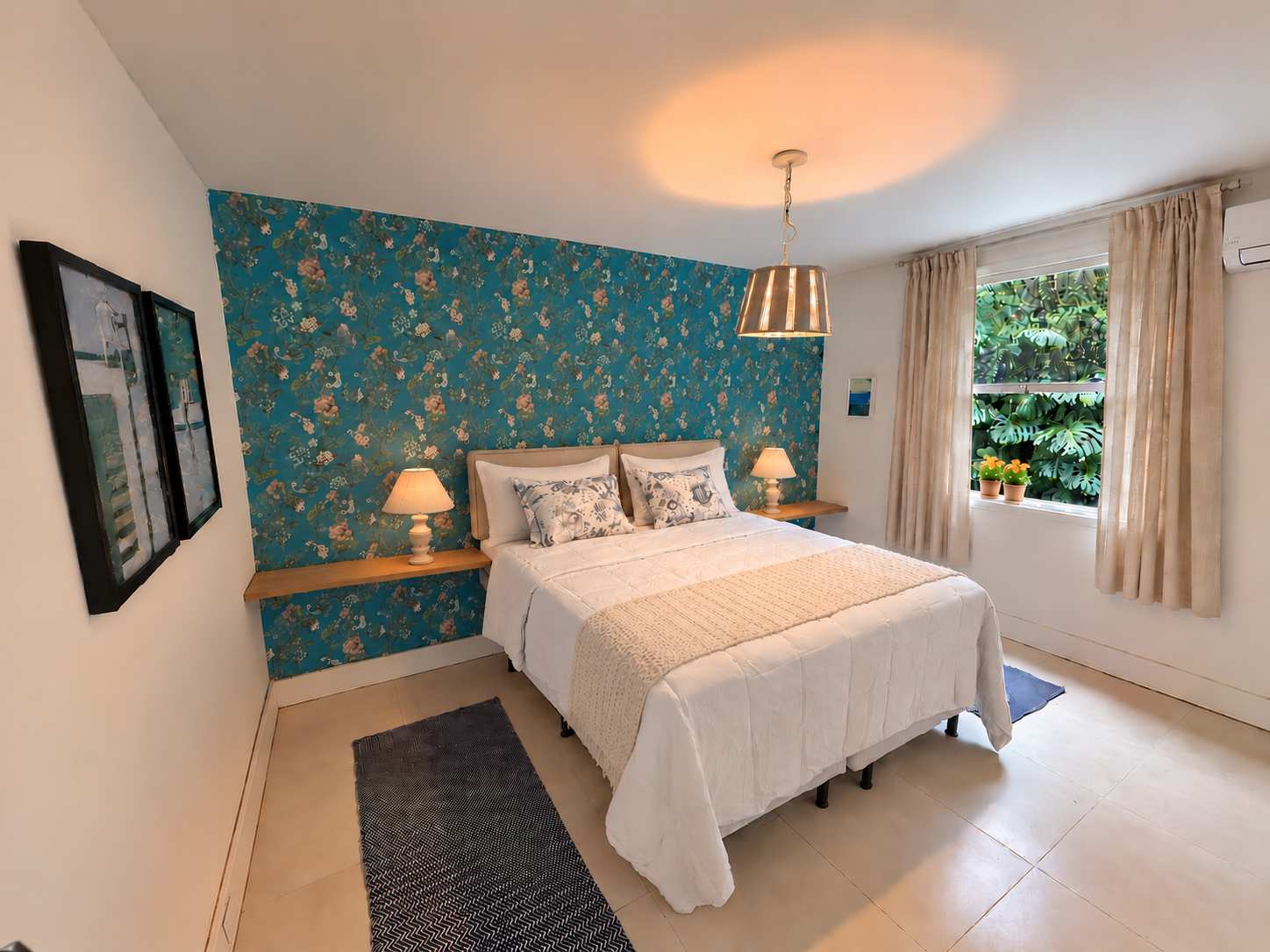 Suíte 06 em plano aberto: cama de casal contra parede de papel azul-petróleo com flores, prateleiras de madeira com abajures e janela para o verde